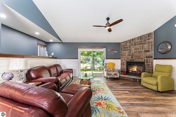 A living room with a fireplace, leather sofas, a green armchair, and a ceiling fan.