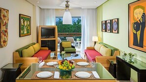 Ein Hotelzimmer mit Essbereich, zwei Sofas mit Kissen, einem Fernseher und Kunstwerken an den Wänden.