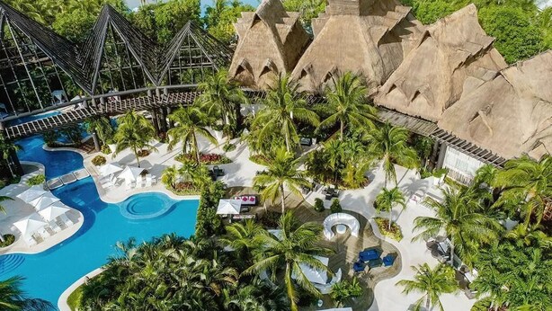 Ein Resort mit großem Pool, Palmen und strohgedeckten Gebäuden.