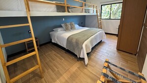 Dormitorio con literas, una escalera de madera, ropa de cama blanca y una ventana con vistas a zonas verdes.