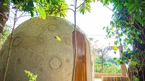 Una estructura abovedada con puerta de madera, rodeada de follaje y un sendero de piedra.