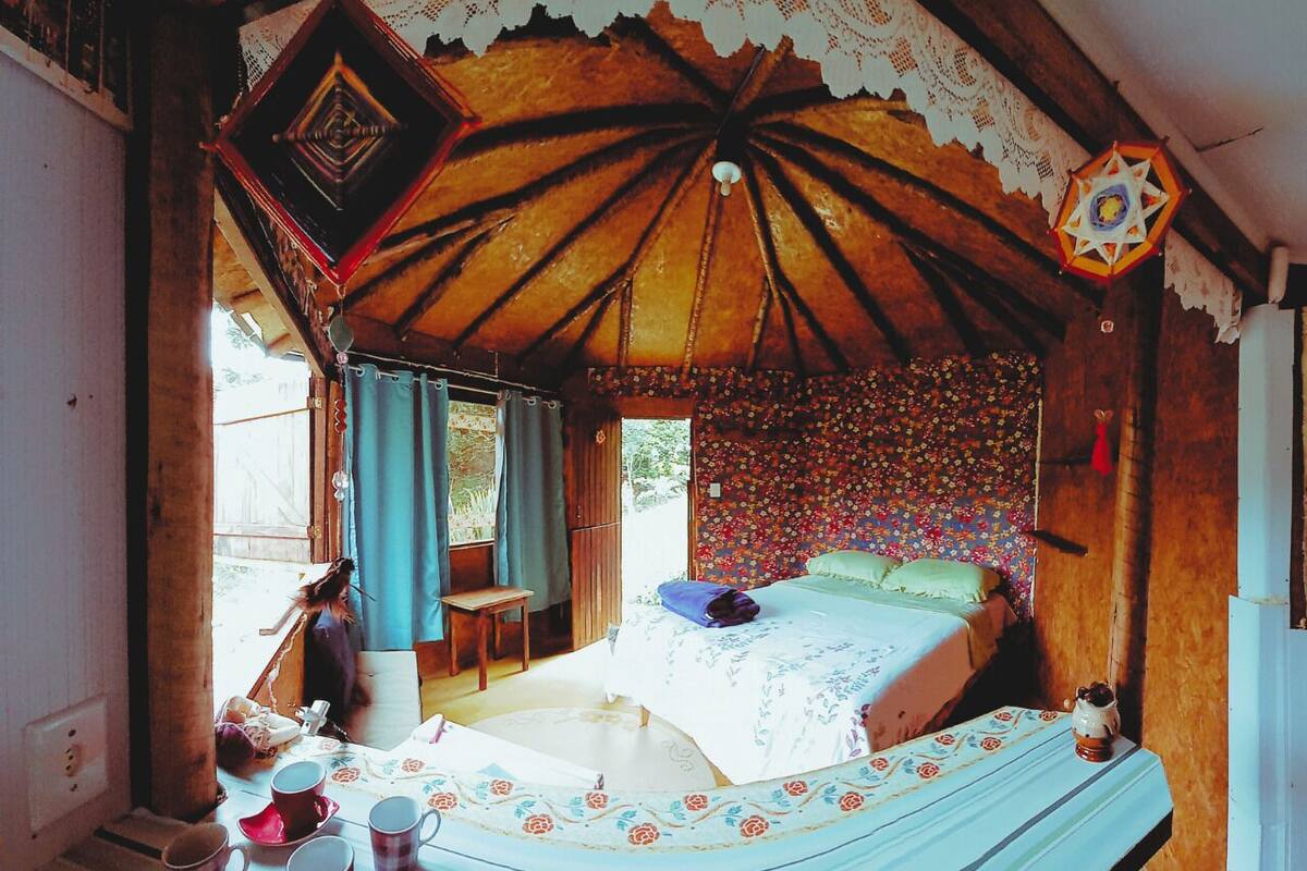 A rustic wooden room with a bed, a table with cups, and a chair.