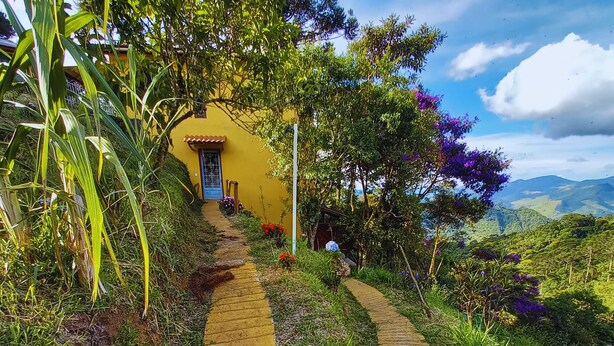 A garden pathway leading to a yellow building with a door, surrounded by lush greenery and flowers.