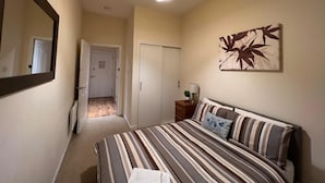 A bedroom with a bed, a nightstand, a lamp, a mirror, and a door leading to another room. - Market Street Aberdeen Apartment (Aberdeen)