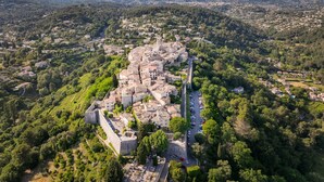 Vista aérea de un pueblo histórico con un castillo destacado, calles estrechas y abundante vegetación.