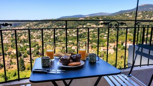 Balcón con una mesa preparada para el desayuno, que incluye pastelería, jugo y una taza, con vistas a un paisaje pintoresco.
