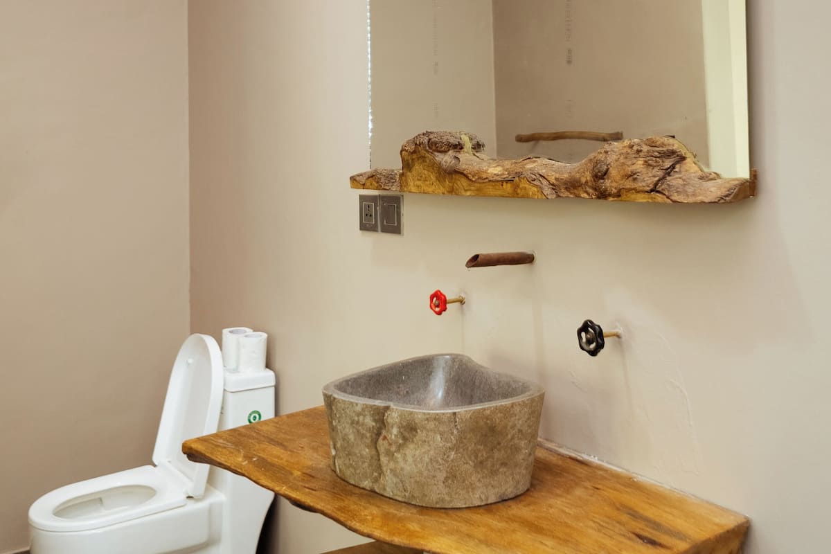 A bathroom with a wooden vanity, a stone sink, a white toilet, and a mirror with a wooden frame.
