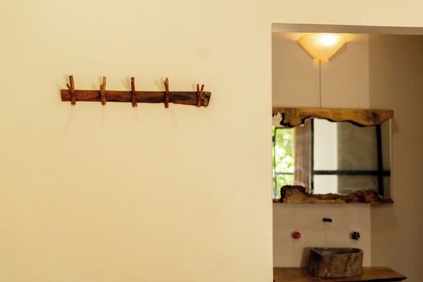 A rustic wooden wall-mounted rack with hooks, a mirror with a natural wood frame, and a stone basin on a wooden table. - Krazy Gecko Resort (Pokhara)