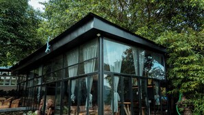A modern glass house with a roof, surrounded by greenery and rocks. - Krazy Gecko Resort (Pokhara)
