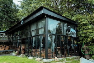 Una casa moderna de vidrio con techo, rodeada de vegetación y rocas.