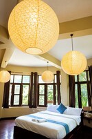 Habitación de hotel con una cama grande, varias lámparas colgantes y ventanas con cortinas.