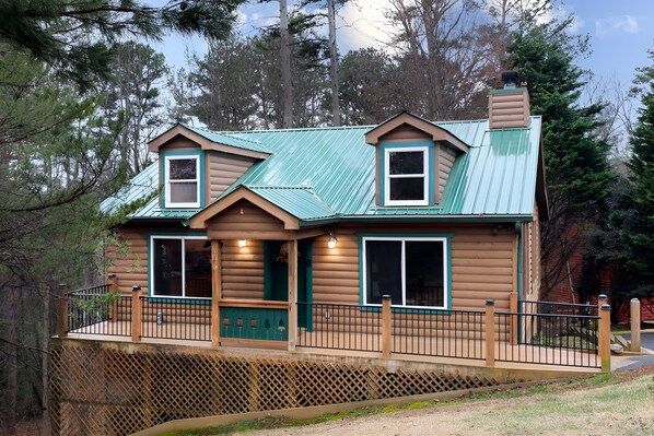 A log cabin with a metal roof, two chimneys, and a wooden deck.
