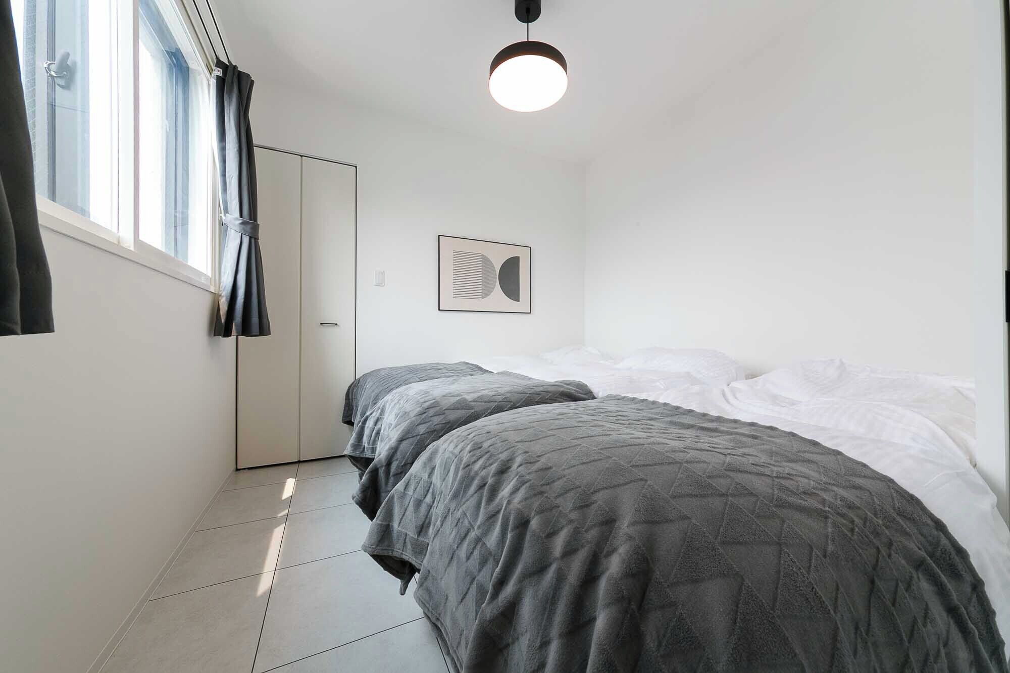 Une chambre avec deux lits, une fenêtre avec des rideaux, un luminaire au plafond et un tableau encadré au mur.