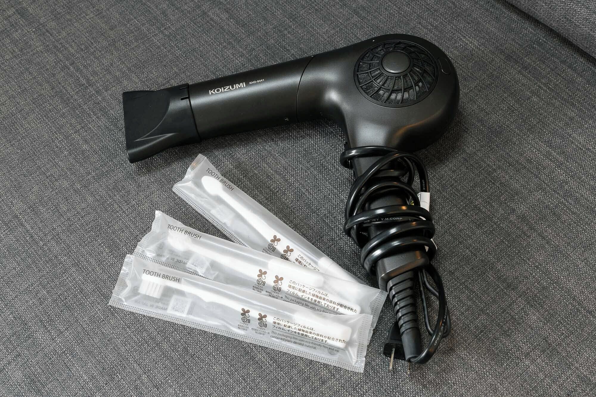 Un sèche-cheveux avec un manche noir et un cordon d’alimentation, ainsi que trois récipients en plastique transparent étiquetés « BROSSE À DENTS ».