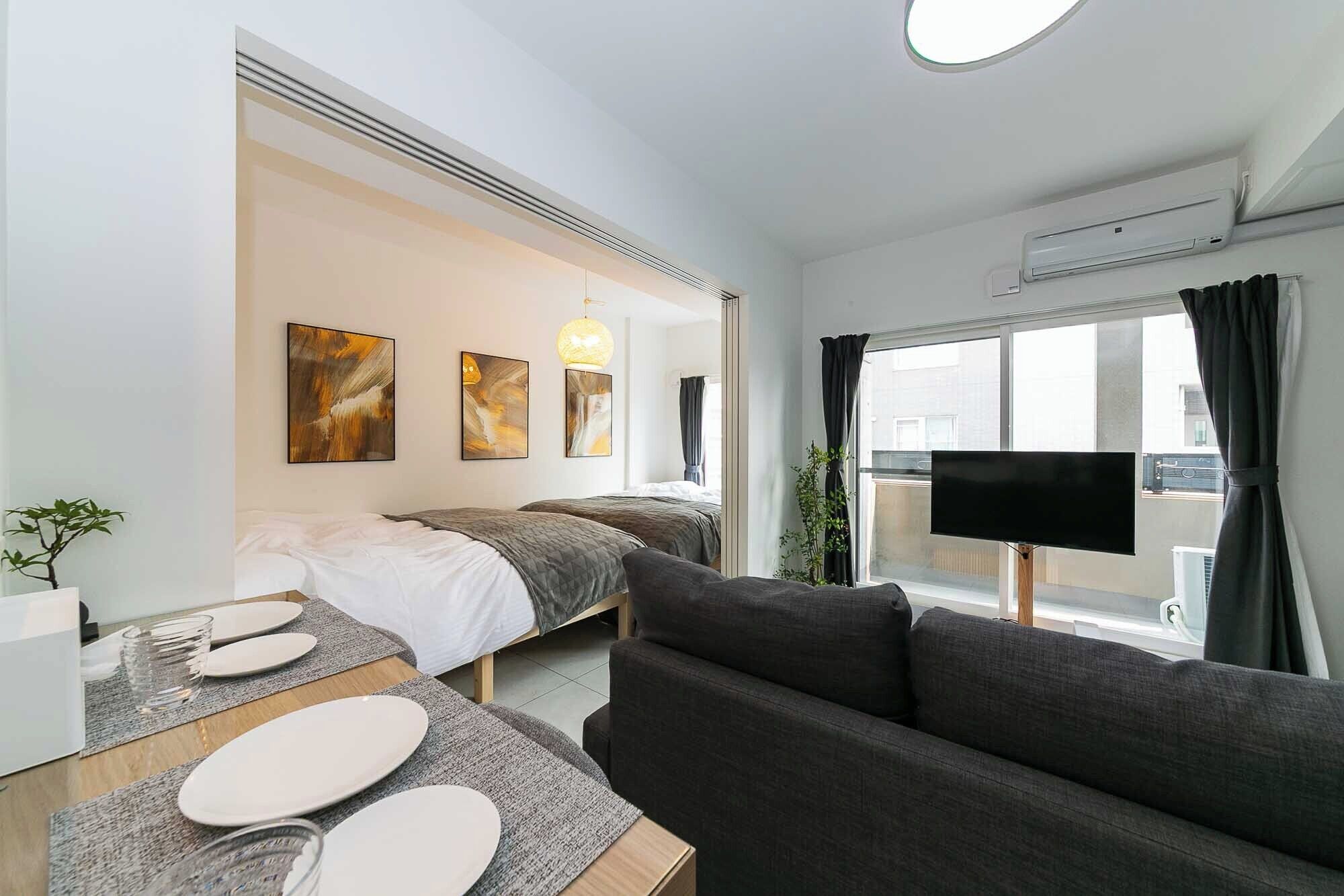 A modern hotel room with a sofa, two beds, a TV, and artwork on the wall.