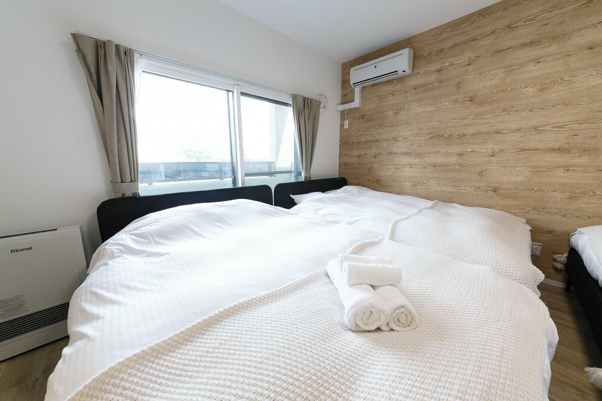 A hotel room with a bed, a window with curtains, an air conditioning unit, and a wooden wall.