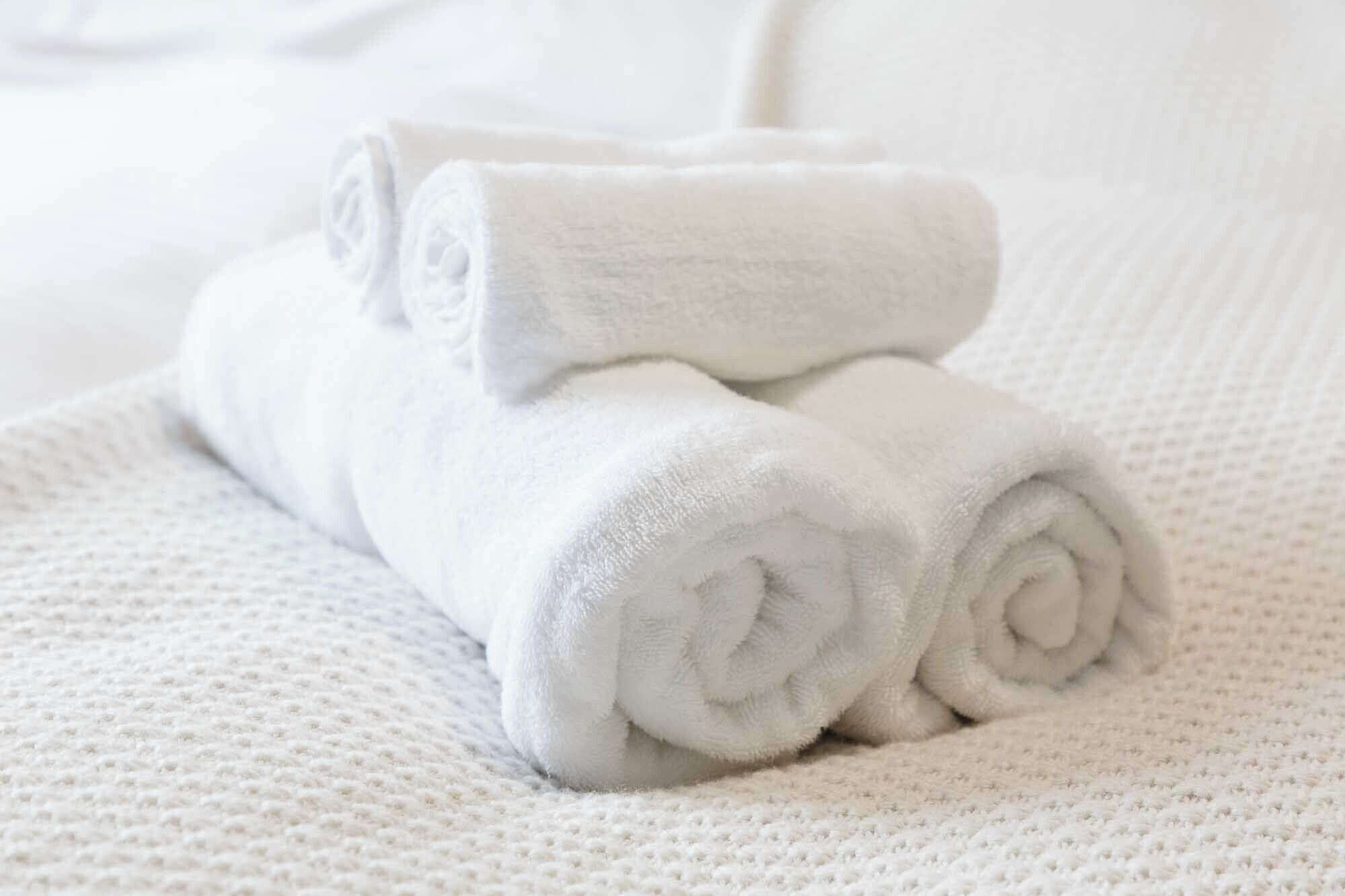 Two neatly rolled white towels stacked on a textured white bedspread.
