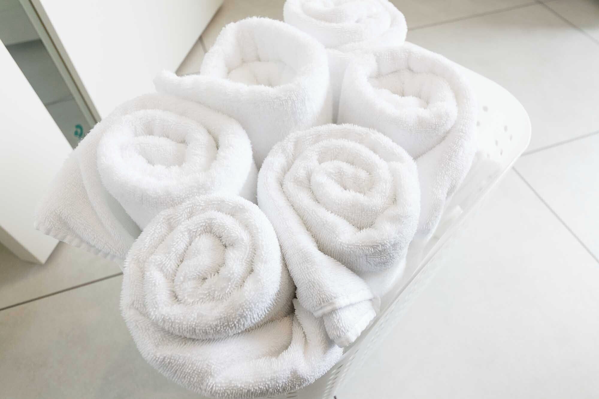 A white towel rack with six neatly rolled white towels.