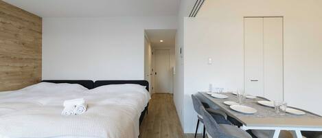 A modern bedroom with a bed, a bedside table, and a dining area with a table and chairs.