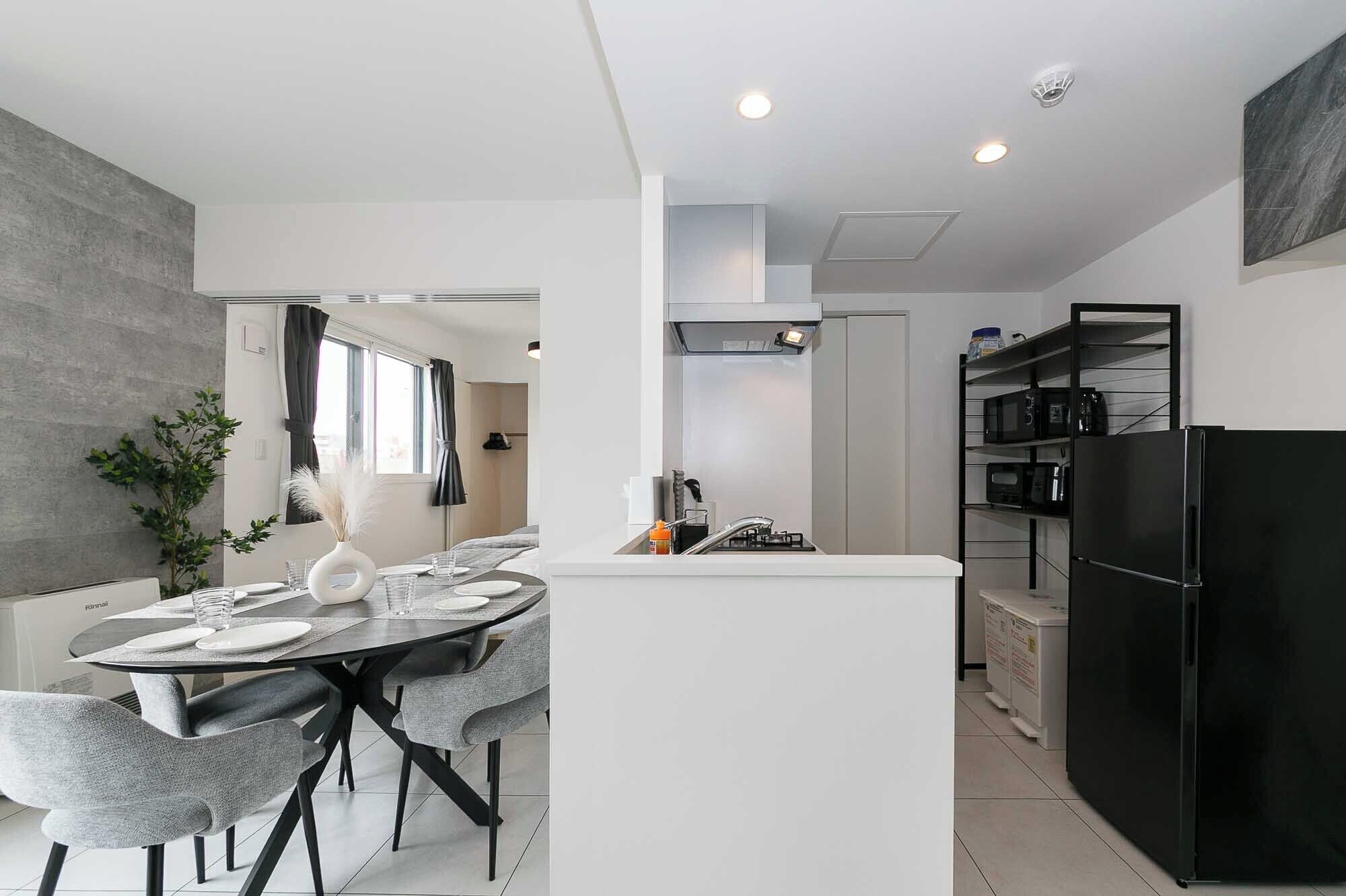 A modern kitchen with a central island, a dining area with grey chairs, and a black refrigerator.