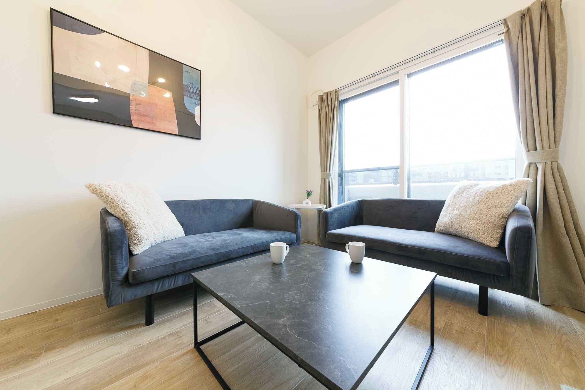 A modern living room with two dark blue sofas, a black coffee table, and a large window with curtains.