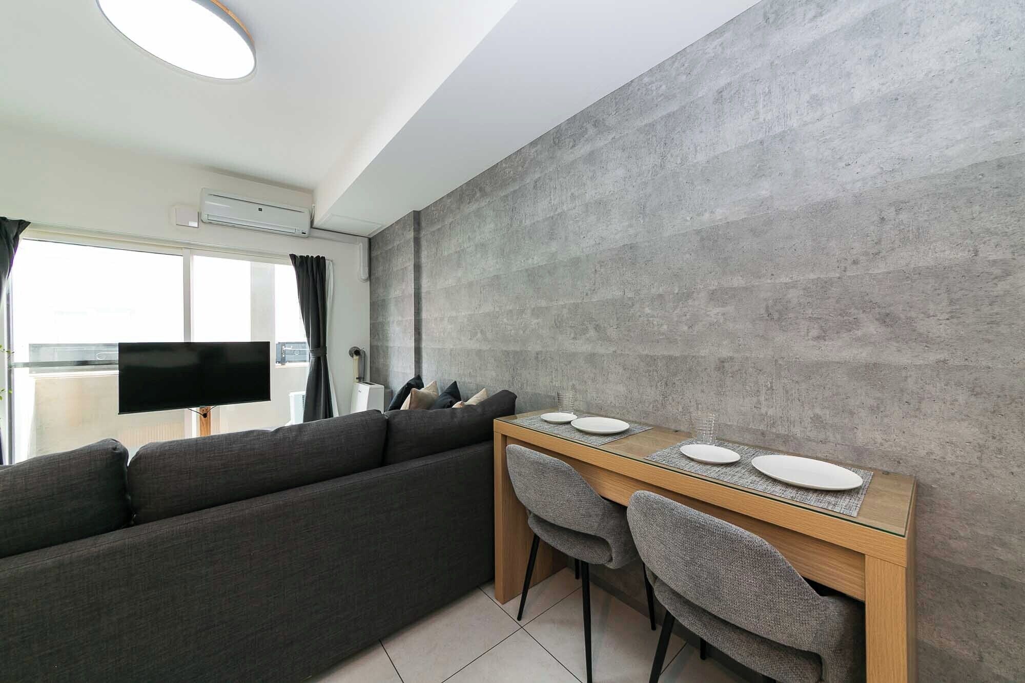 Een moderne woonkamer met een grijze bank, een houten eettafel met twee stoelen en een groot raam met gordijnen.