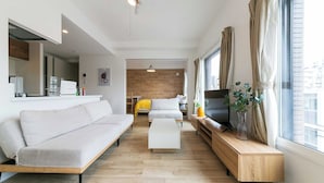 A modern living room with a sofa, coffee table, and TV stand. There is a wooden accent wall and a large window with curtains. - EFFECT minami7 (Sapporo)