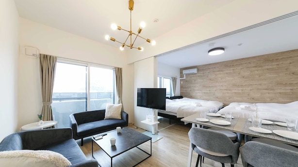 A modern hotel room with a sofa, a coffee table, a TV, a bed, and a dining area with a table set for two. - EFFECT minami7 (Sapporo)