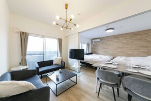 A modern hotel room with a sofa, a coffee table, a TV, a bed, and a dining area with a table set for two. - EFFECT minami7 (Sapporo)