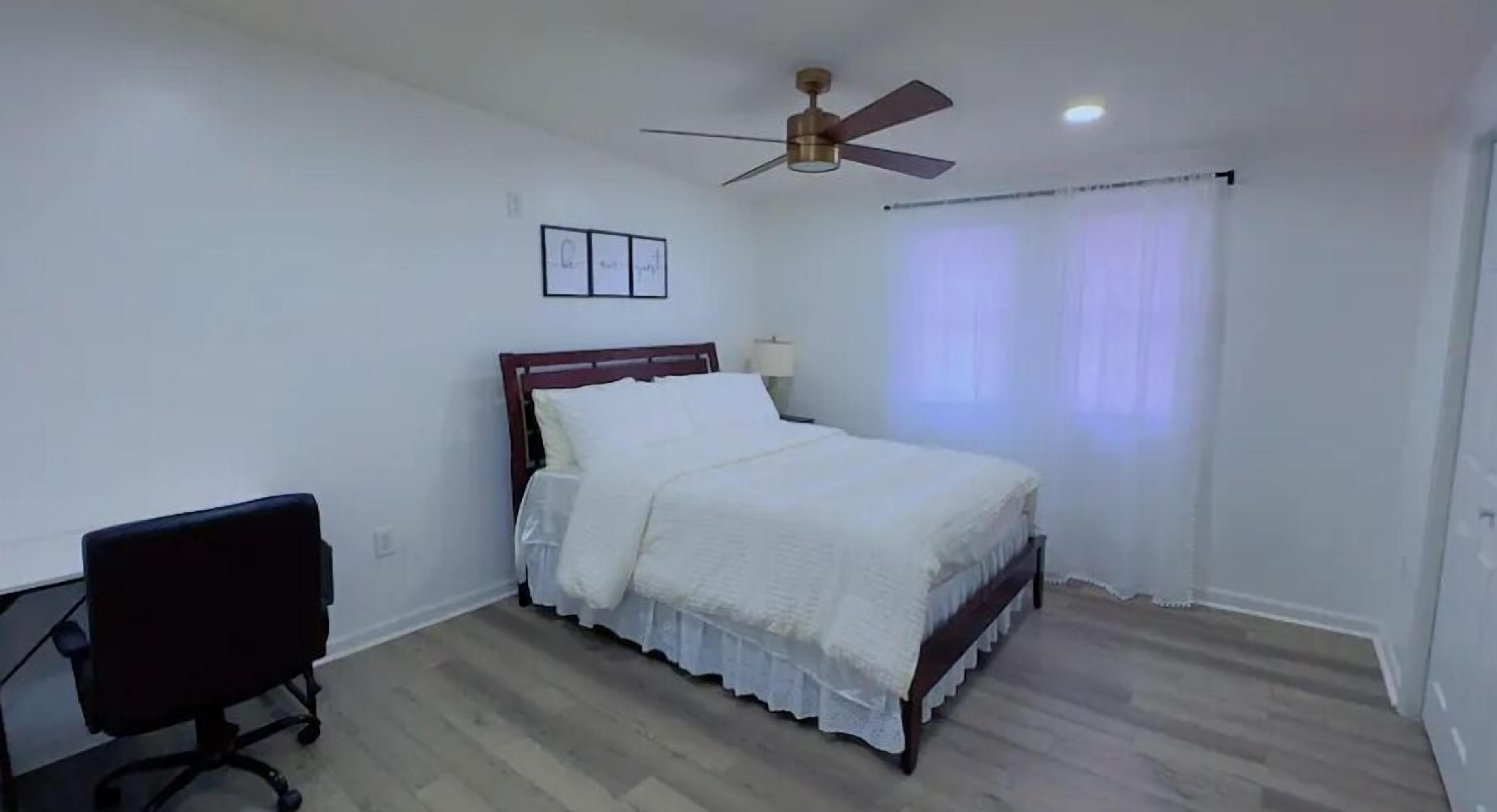 A bedroom with a bed, a desk, and a ceiling fan.