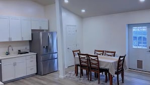 A modern kitchen with white cabinets, a stainless steel refrigerator, and a dining area with wooden chairs and a table. - Quiet 2BR-Retreat Near Alum Creek & Lewis Center (Delaware)