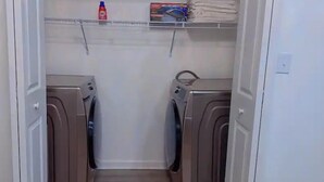 A laundry room with two washing machines, a shelf with folded towels, and a bottle of detergent. - Quiet 2BR-Retreat Near Alum Creek & Lewis Center (Delaware)