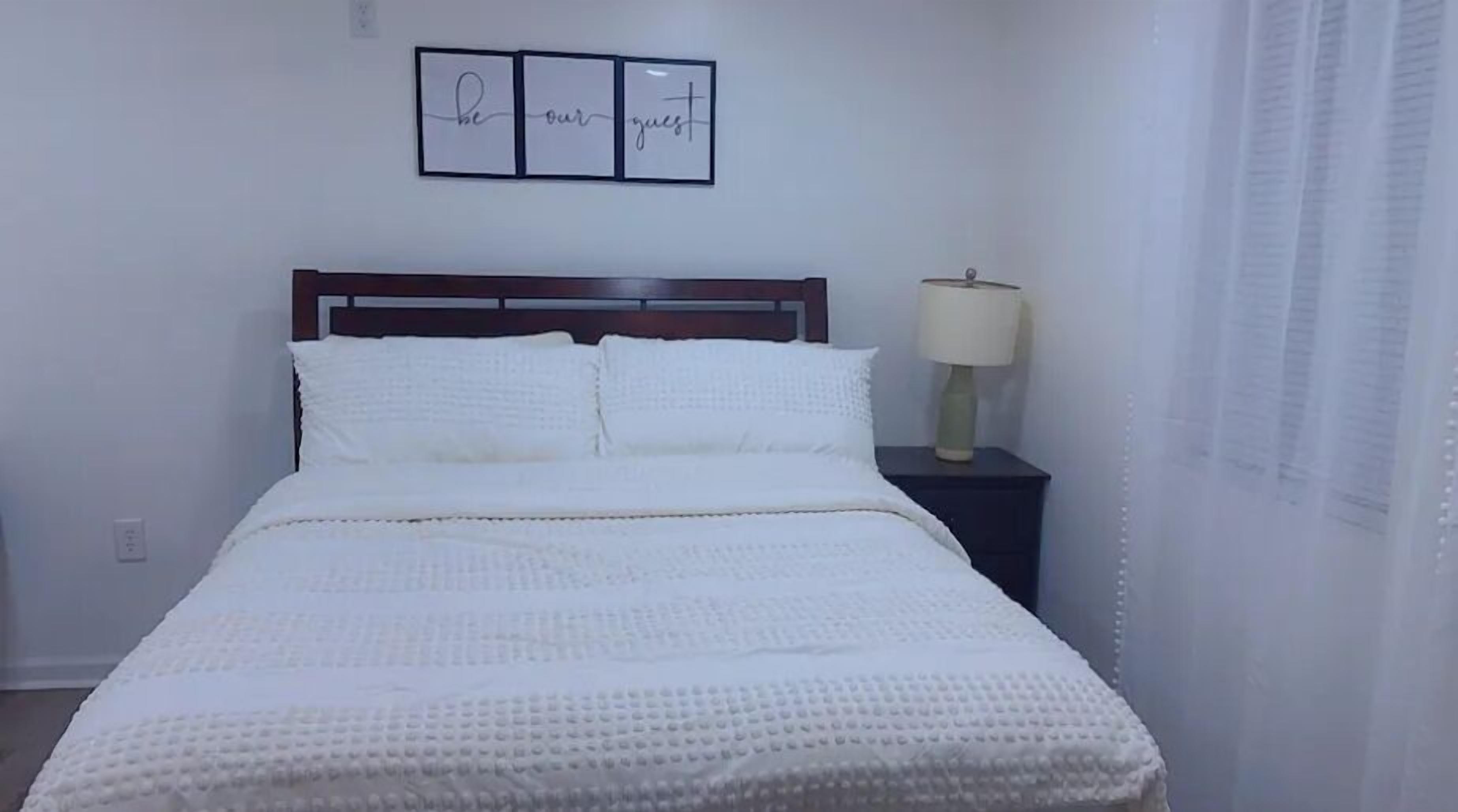 A neatly made bed with white bedding, a dark wooden headboard, and a bedside table with a lamp.