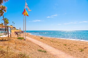 Ein Strand mit blauem Himmel, einem Sandweg und einem Fahnenmast mit Flaggen.