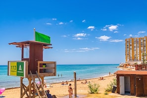 A lifeguard tower with a green flag, a beach with people, and a building with balconies. - Calahonda Beach A, Mijas Costa, Spain (Mijas Costa)