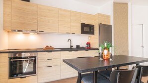 A modern kitchen with wooden cabinets, a built-in oven, a microwave, and a refrigerator. There is a dining table with chairs and a bottle of wine. - Calahonda Beach A, Mijas Costa, Spain (Mijas Costa)