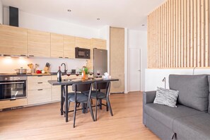 Una cocina moderna con armarios de madera, una mesa de comedor con sillas, un refrigerador y un sofá gris con un cojín a rayas.