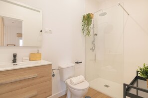 A modern bathroom with a white toilet, a wooden vanity, a glass shower enclosure, and a mirror above the vanity.