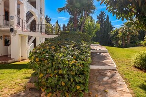 Un jardin bien entretenu, avec un chemin de pierre menant à un bâtiment à la façade blanche et doté d’un balcon.