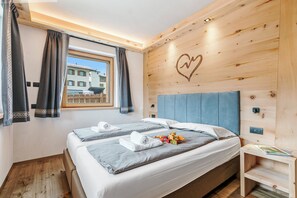 A bedroom with two beds, a wooden headboard with a heart design, a window with curtains, and a nightstand with a magazine.