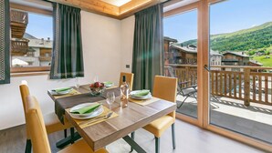 A dining area with a table set for four, chairs, a view of a mountainous landscape through large windows, and a balcony with a wooden railing. - Livia, Livigno, Italy (Livigno)