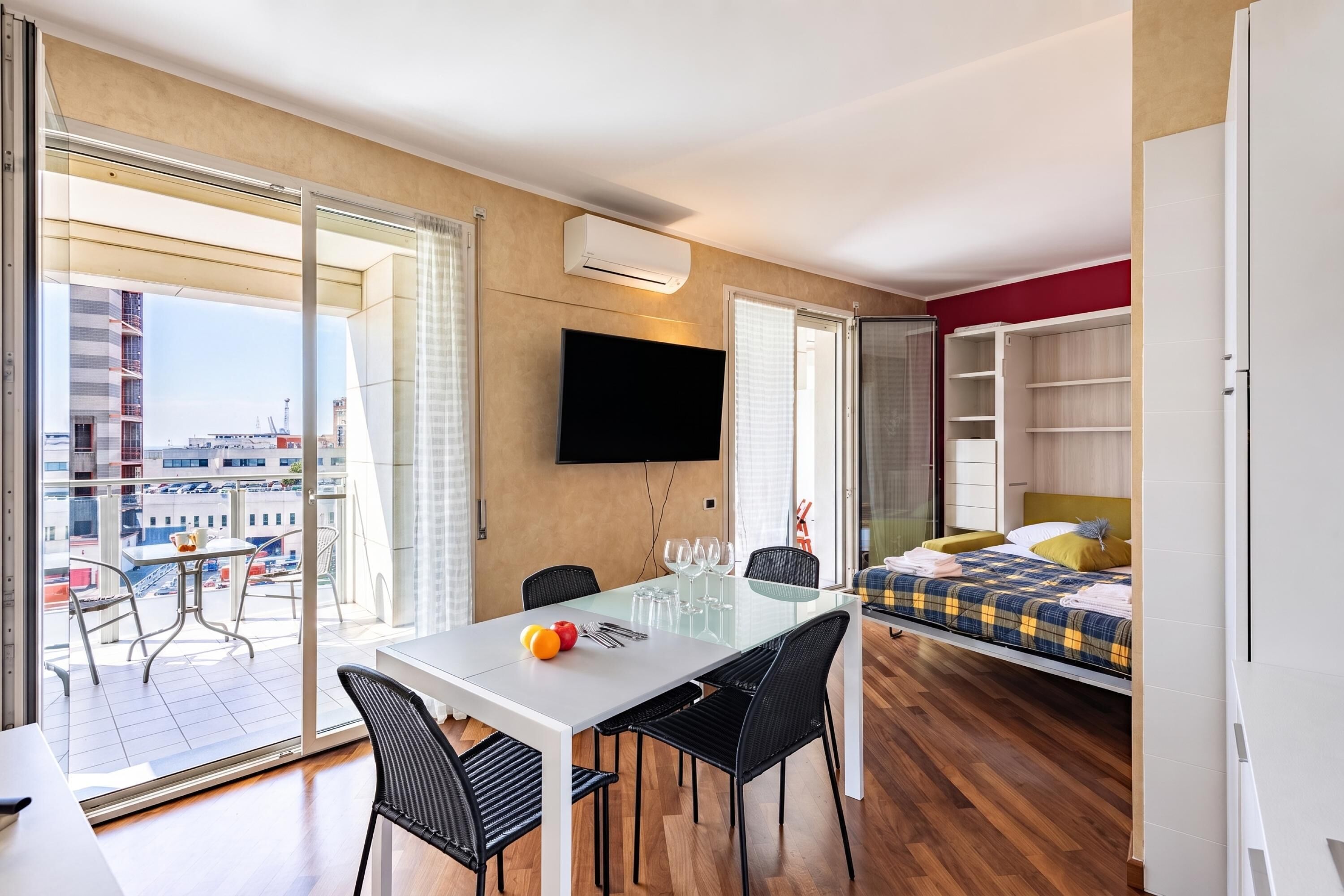 Moderni hotellihuone, jossa on parveke, ruokailutila, sänky ja televisio.