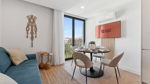 Moderni hotellihuone, jossa on sohva, ruokapöytä tuoleineen, suuri ikkuna, josta on näkymä, ja kyltti, jossa lukee ”VALMIS VASTAANOTTAMAAN VIERAITA”.