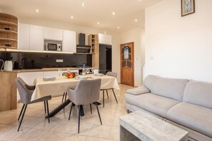 A modern kitchen with white cabinetry, a dining table set for four, and a grey sofa in a living area. - Sea and Silence Apt /w Sea View Balcony, Lopar, Croatia (Lopar)