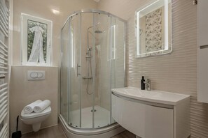 A modern bathroom with a glass shower enclosure, a toilet, a sink, and a window with a view.