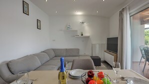 A modern living room with a dining table set for two, a grey sofa, a TV, and a small shelf with decorative items. - Sea and Silence Apt /w Sea View Balcony, Lopar, Croatia (Lopar)