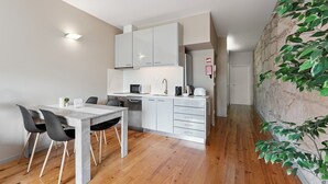 Une cuisine compacte avec des meubles blancs, une table à manger avec des chaises et un plancher en bois.
