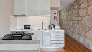 Une cuisine compacte avec des meubles blancs, un four à micro-ondes, une machine à café et un mur en pierre.