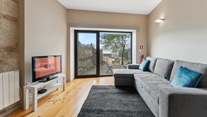 Un salon moderne avec un canapé gris, un téléviseur à écran plat et une porte-fenêtre coulissante donnant sur un espace extérieur.