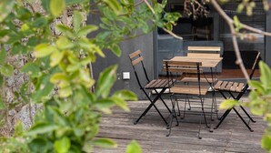 Un espace extérieur aménagé pour les repas, avec une table et des chaises, un mur en pierre et de la verdure au premier plan.